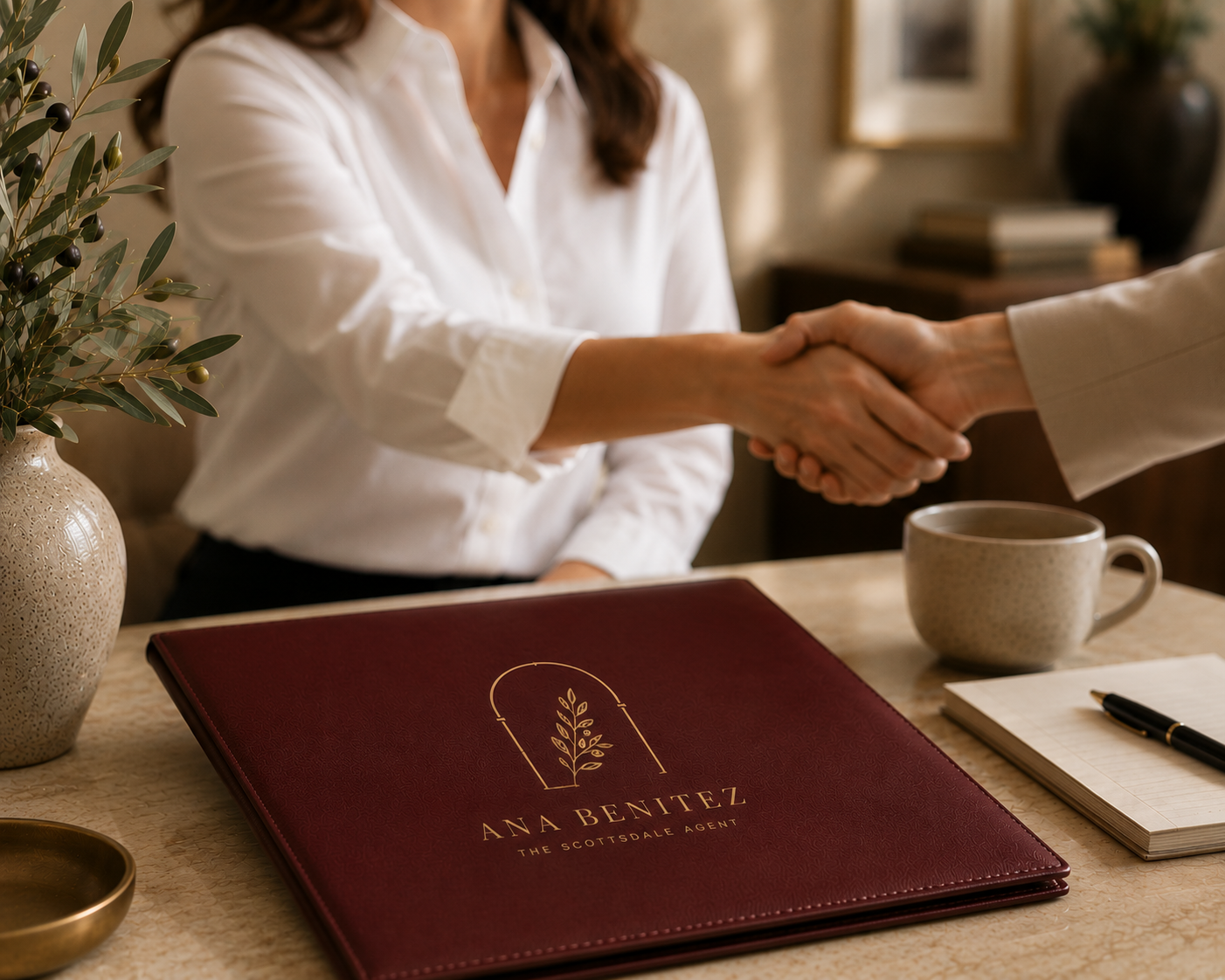 A handshake over an Ana Benitez branded burgundy presentation folder.